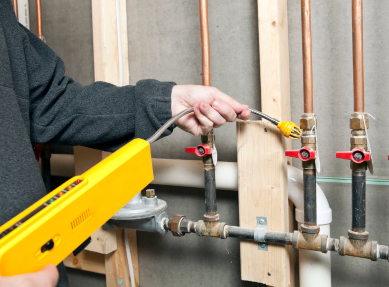 Person using a yellow tester on exposed plumbing pipes and valves in a wall cavity