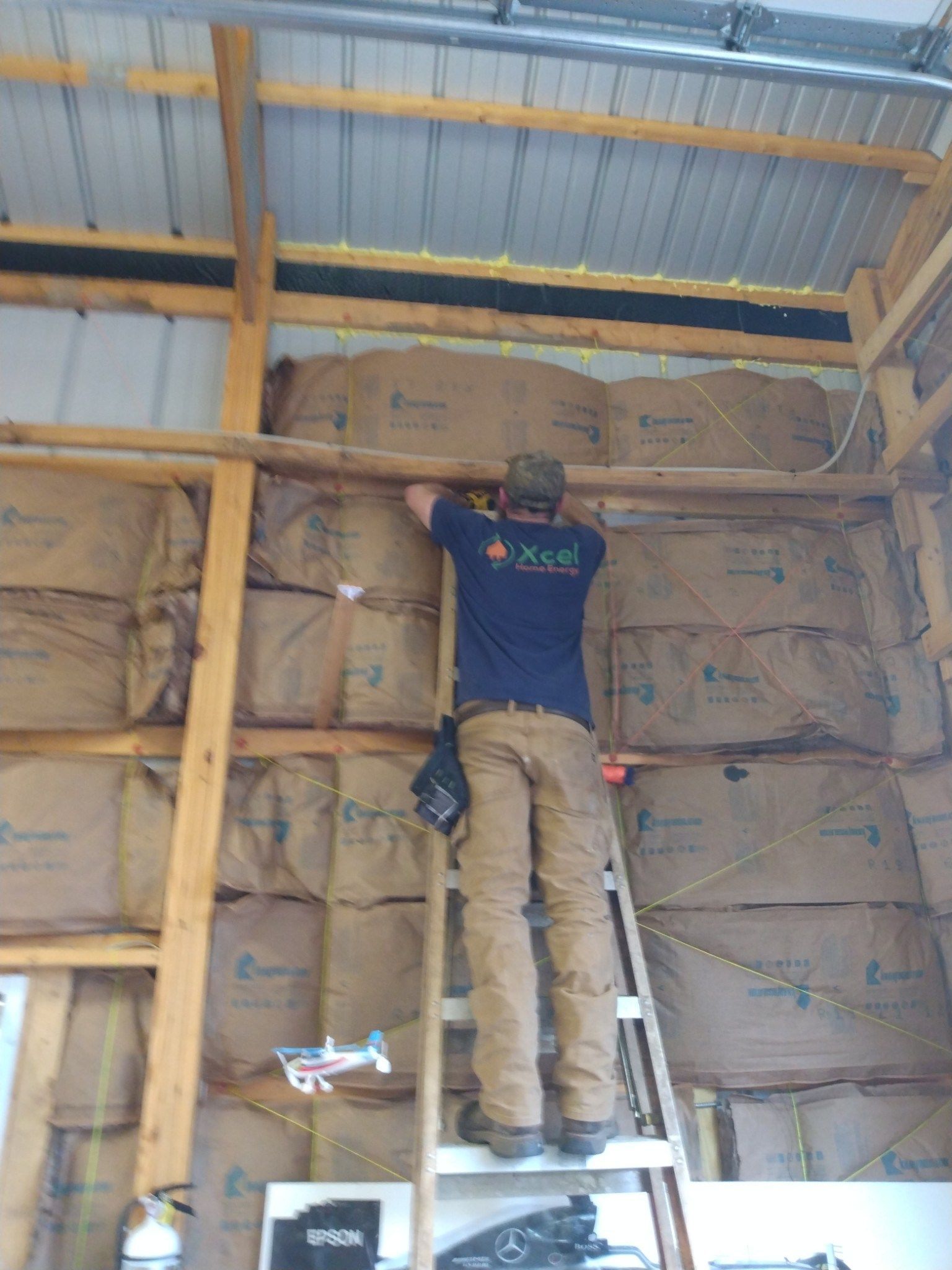 Worker installing insulation inside a wooden-framed wall under a metal roof
