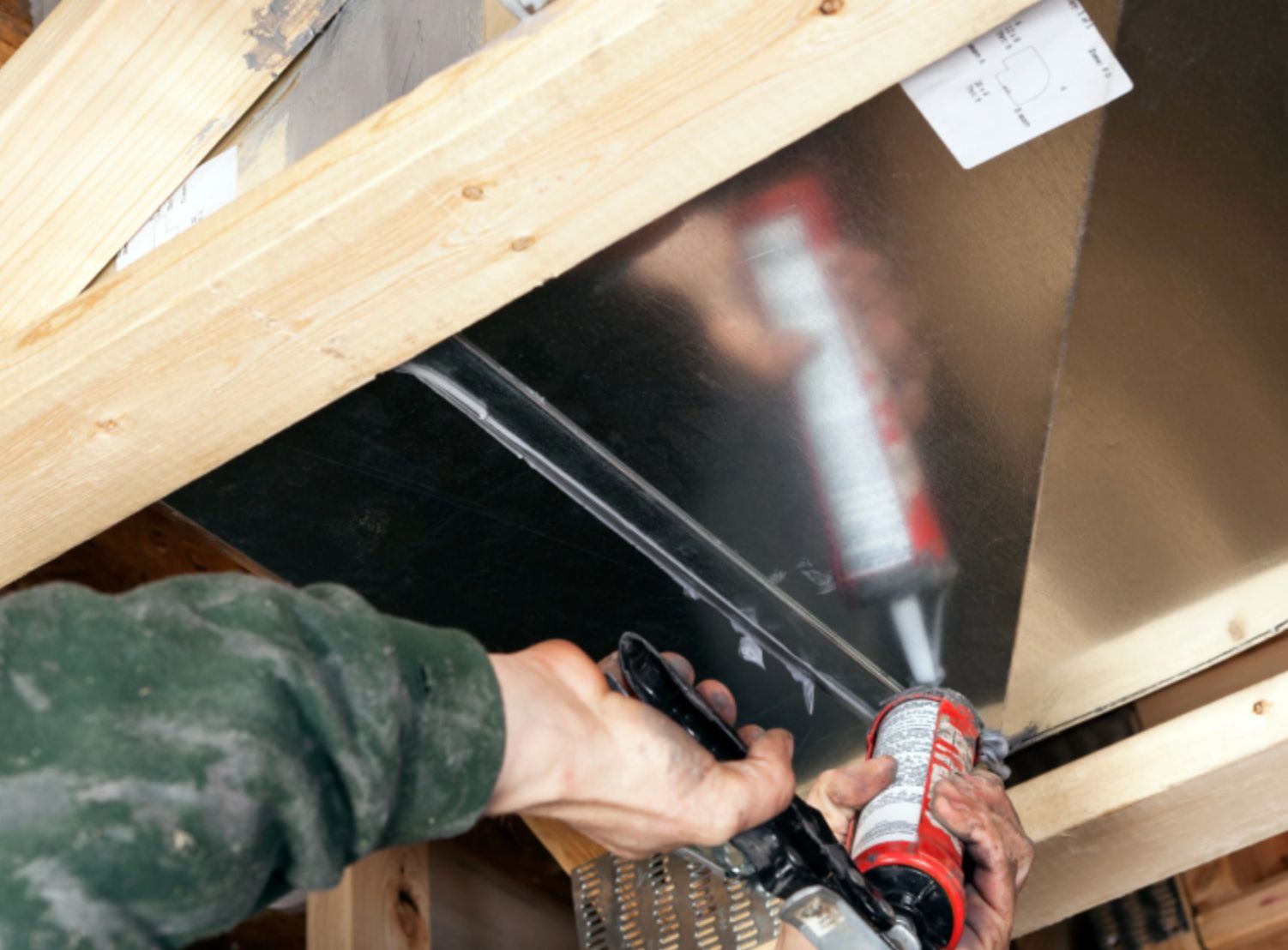 Person using a caulking gun to seal a joint in a wooden structure under construction
