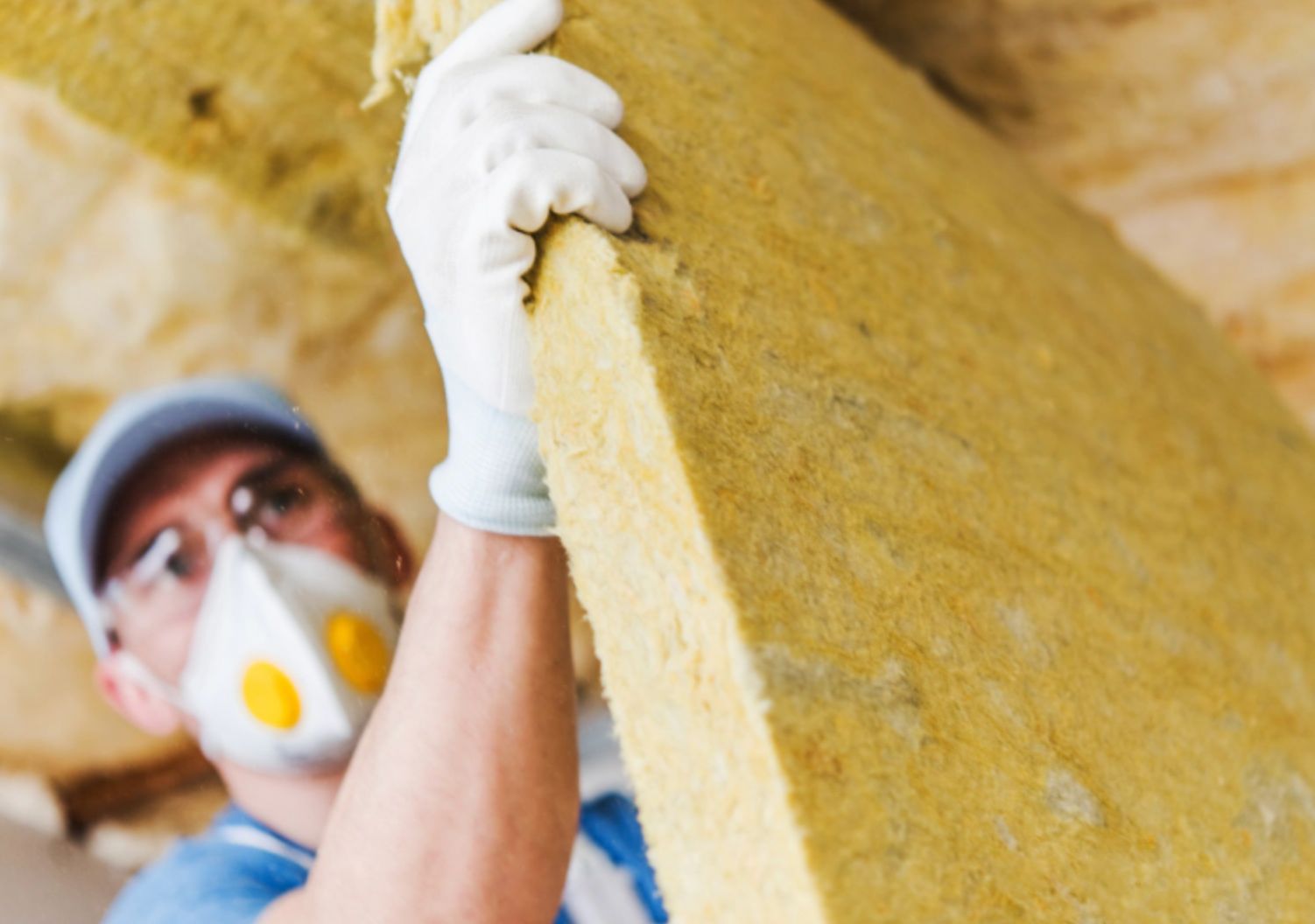 Worker installing yellow insulation board, wearing gloves and a respirator mask