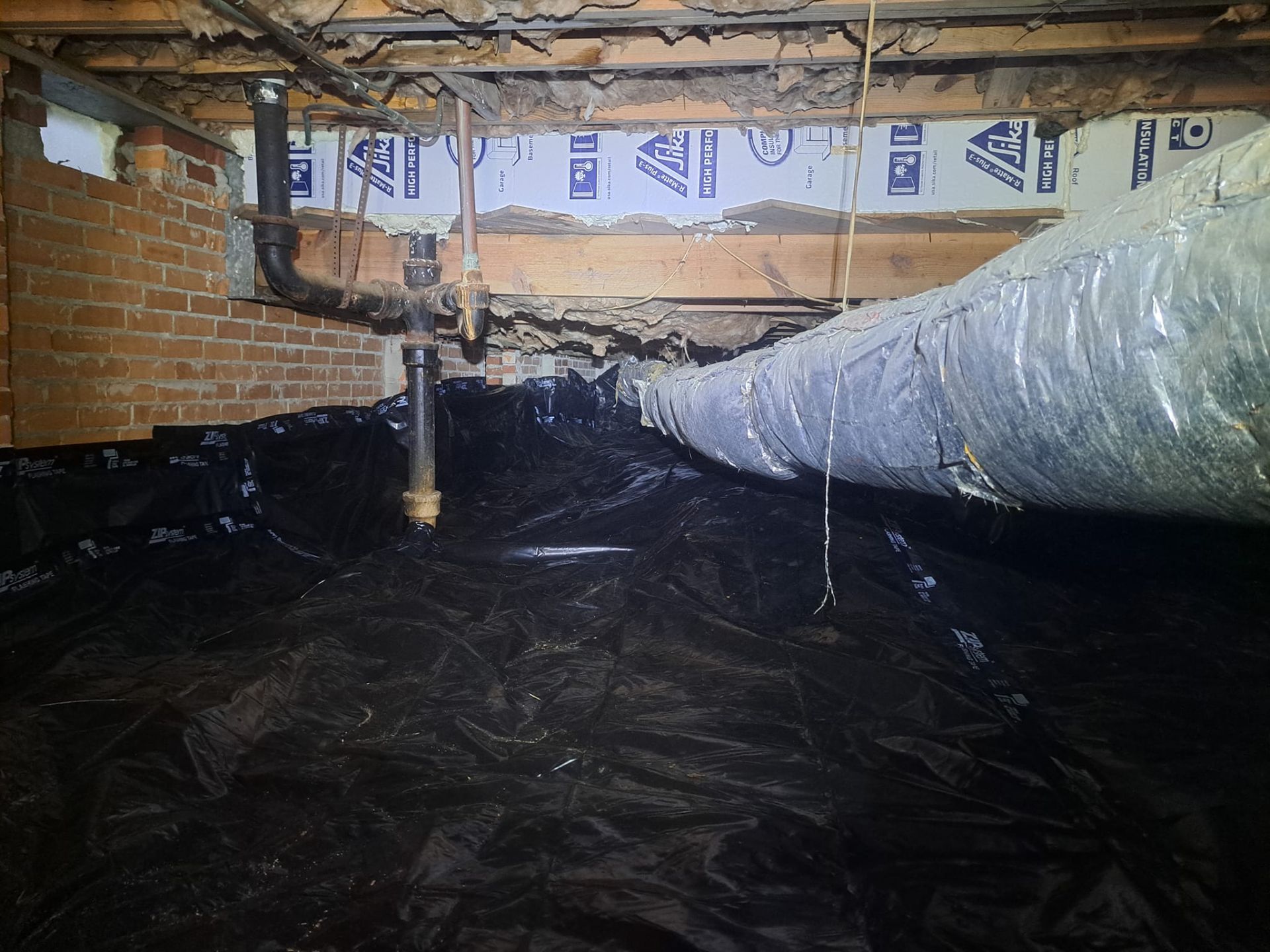 Brick crawlspace with black plastic vapor barrier and a large insulated duct running overhead