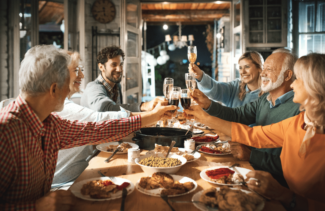 Friends sharing a festive meal and toasting drinks around a long table in a cozy restaurant