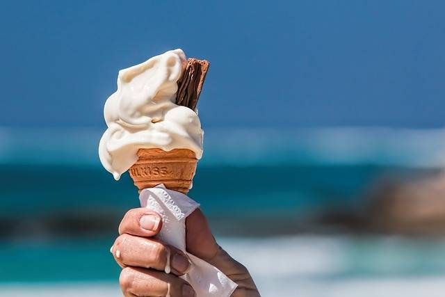Hand holding a vanilla ice cream cone with blue ocean and sky in the background