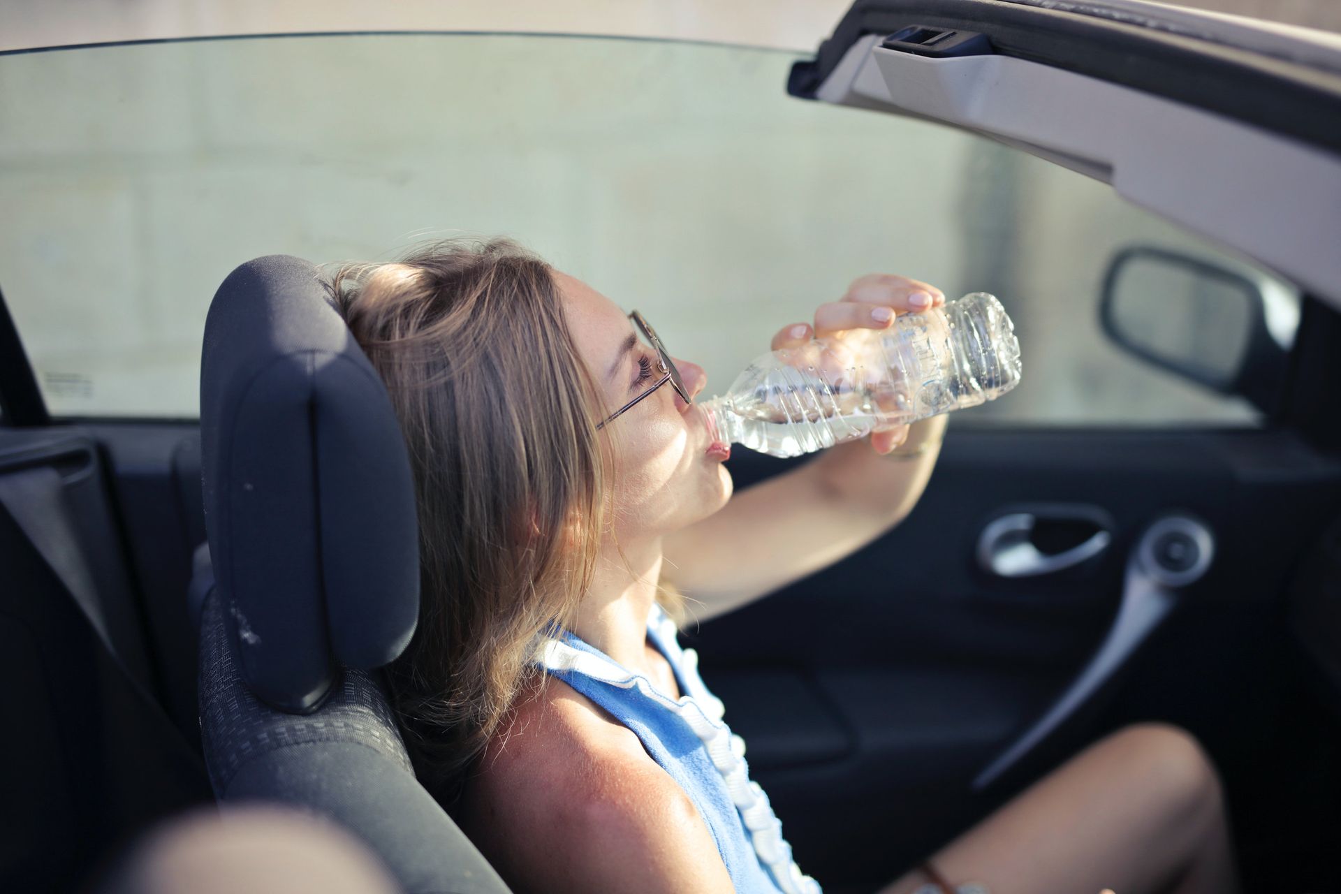 Passenger drinking from a water bottle in a car seat with the window down