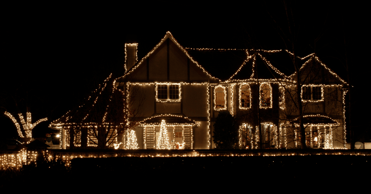 House outlined with warm white holiday lights at night, with lit trees on the lawn