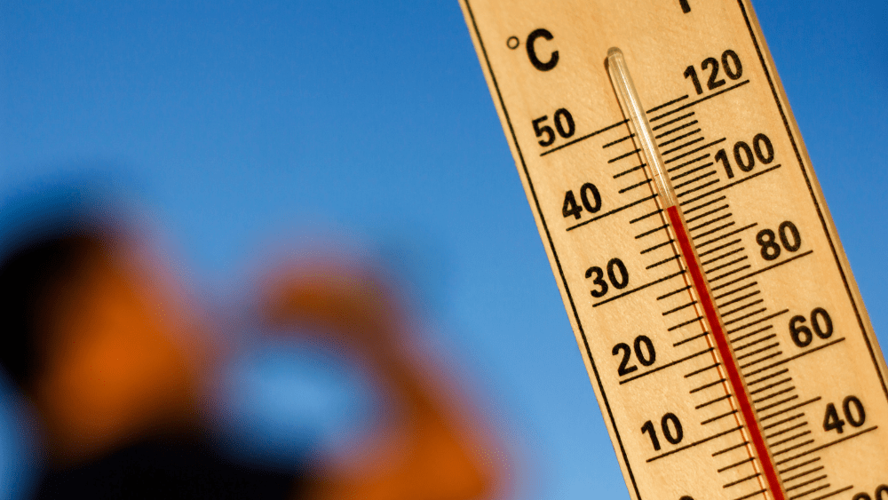 Close-up of a thermometer showing hot temperatures against a blurred blue sky and sunlit background