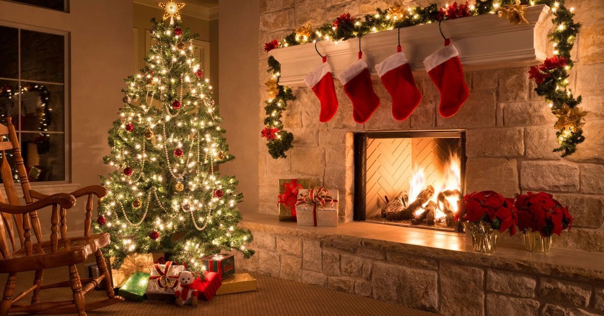 Cozy living room with lit Christmas tree, fireplace, stockings, and wrapped gifts in warm glow