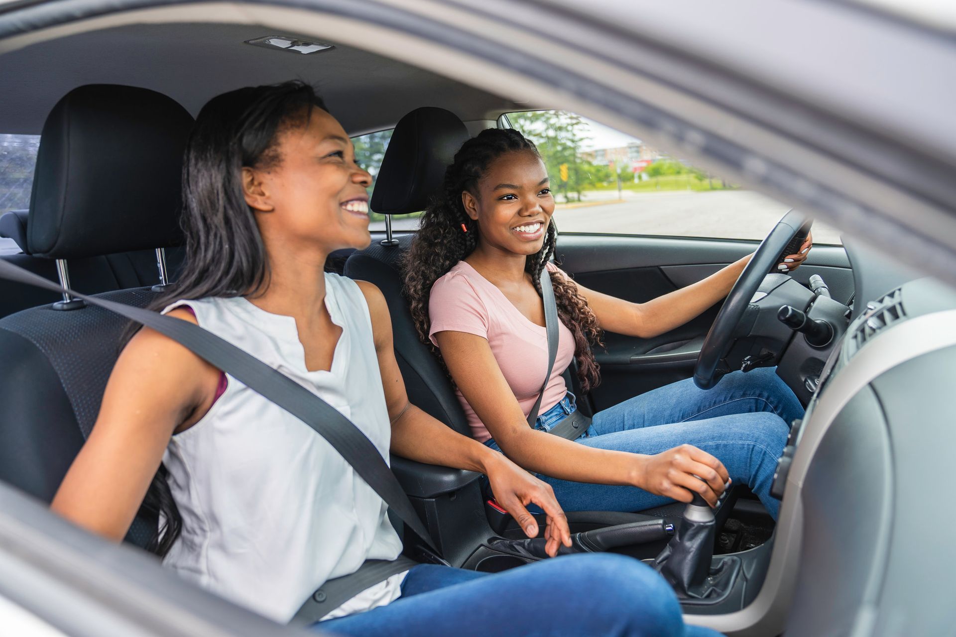 Two people smiling in a car, one driving and one in the passenger seat with seatbelts on