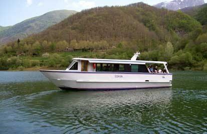Barca passeggeri bianca su un lago tranquillo con verdi montagne sullo sfondo.