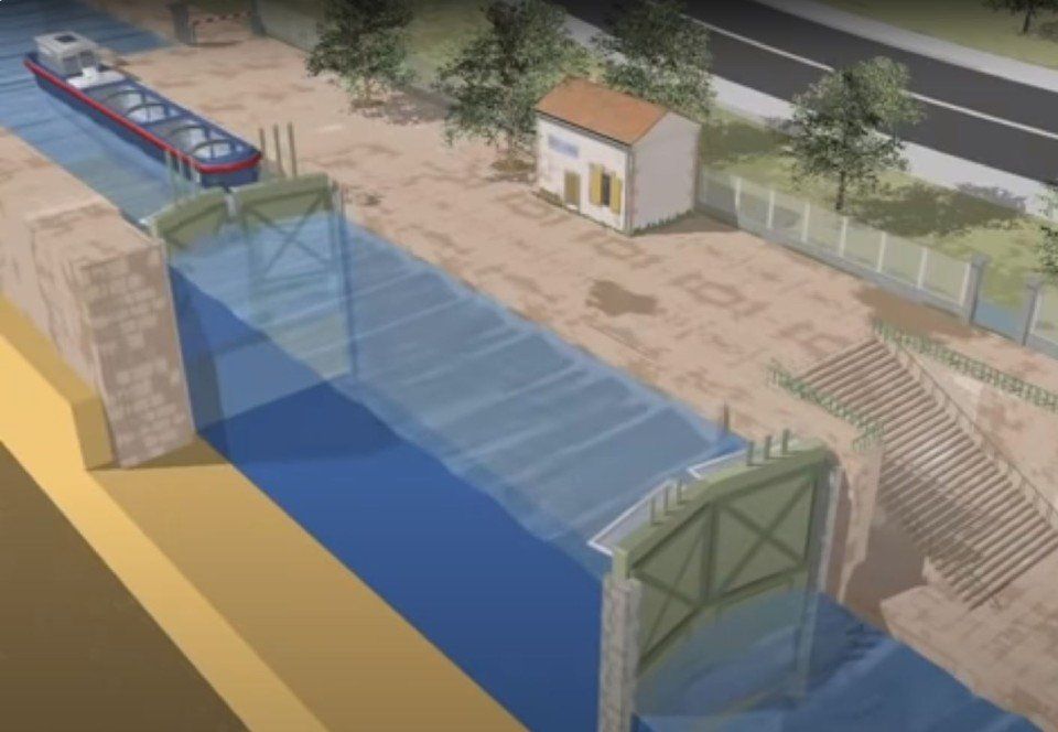 Veduta aerea di una barriera blu contro le inondazioni che blocca l'acqua a lato di una strada e di un canale, vicino a un piccolo edificio.
