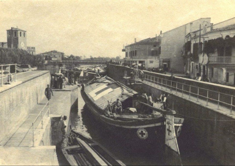 Scena vintage di un canale con una barca in uno stretto corso d'acqua fiancheggiato da edifici e muri.