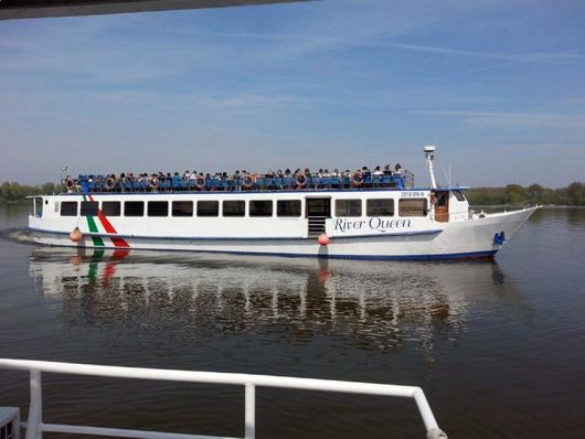 Traghetto passeggeri bianco con persone sul ponte, che naviga su acque calme sotto un cielo limpido.