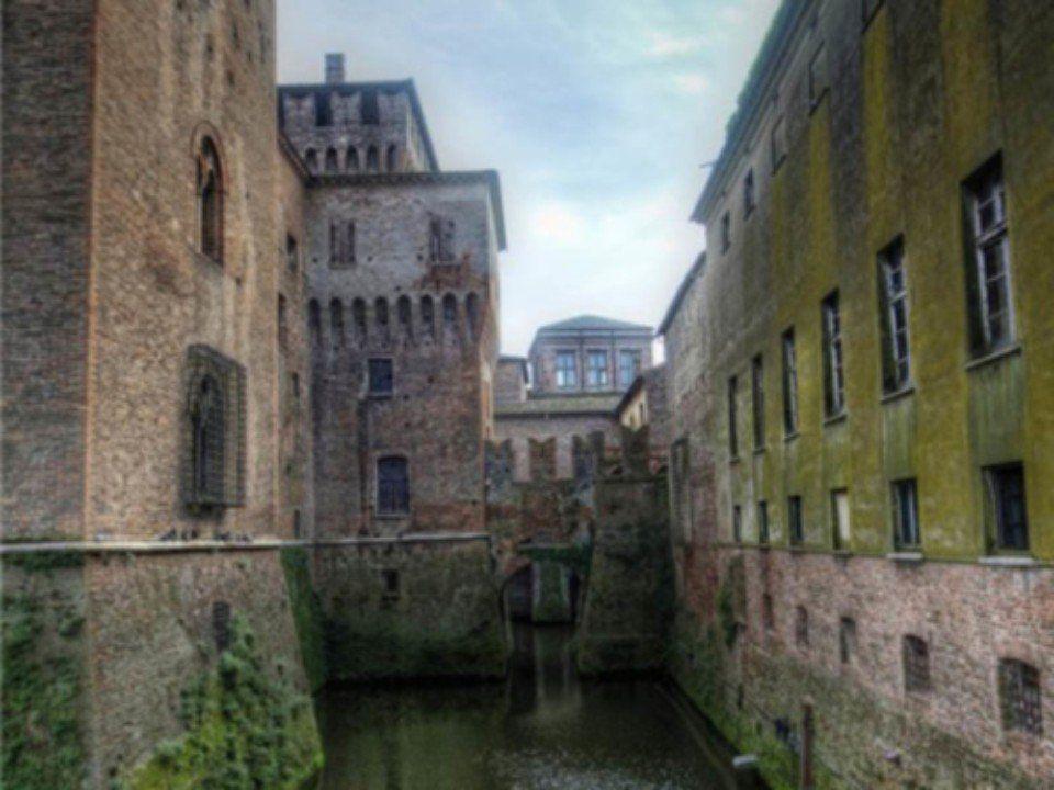 Uno stretto canale tra antichi edifici in pietra, con muri consumati dal tempo e un cielo nuvoloso sopra.