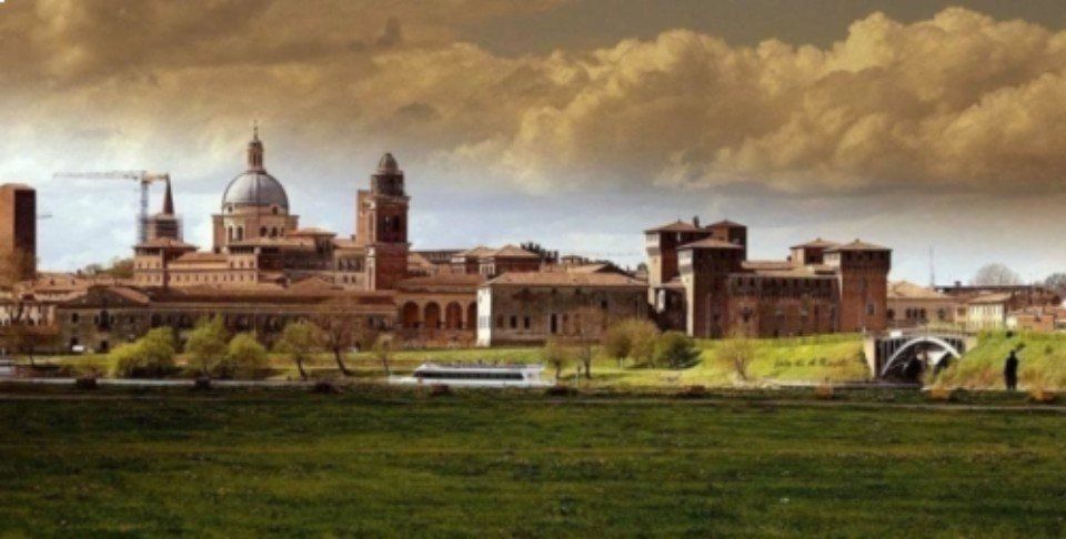 Panorama storico della città con edifici a cupola e torri sotto un cielo nuvoloso, visto attraverso campi verdi.