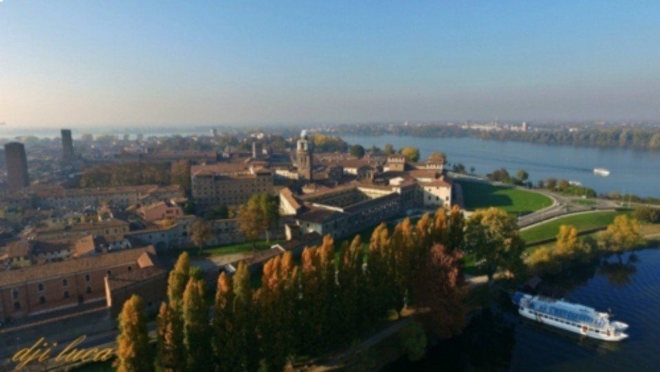 Veduta aerea di una storica città fluviale con un ponte, una strada tortuosa e barche sull'acqua al tramonto.