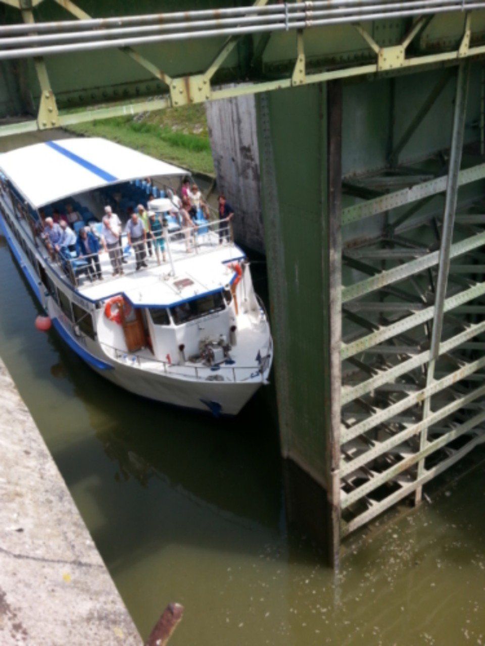 Barca turistica che attraversa uno stretto canale accanto a un ponte verde di supporto