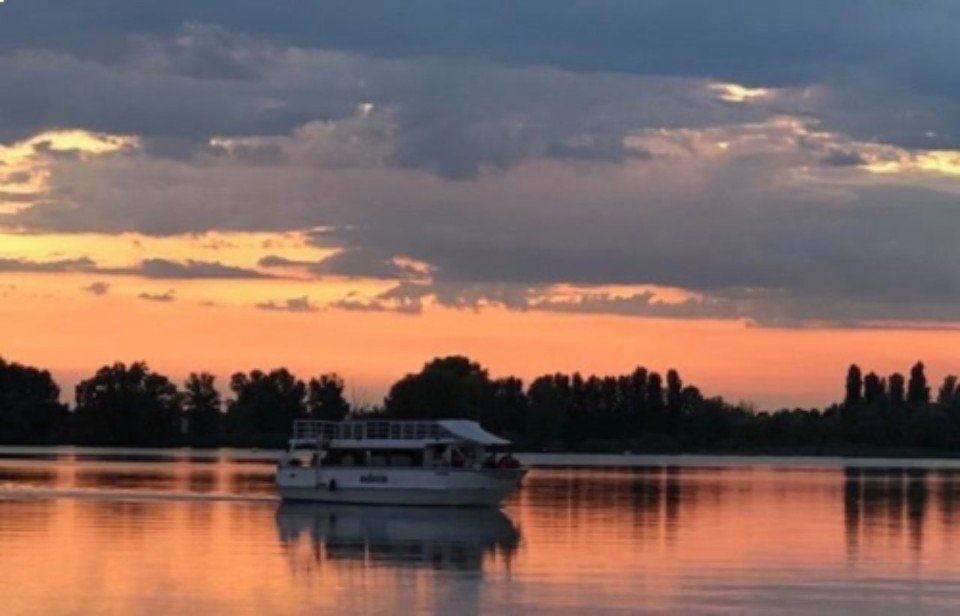 Barca su un lago tranquillo al tramonto, con cielo arancione e alberi in controluce che si riflettono nell'acqua.