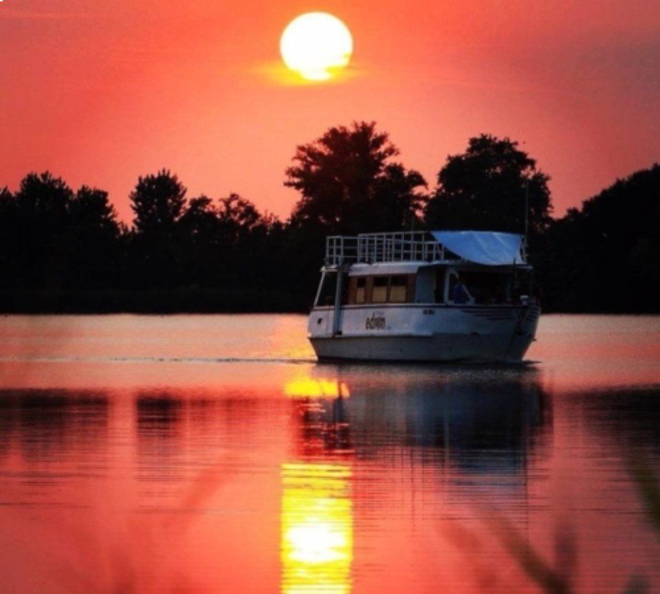 Una barca su un lago tranquillo al tramonto, con un cielo di un arancione intenso che si riflette sull'acqua.