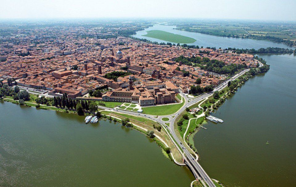 Veduta aerea di una città storica situata su una penisola, con ponti, circondata dall'acqua e con un fiume in lontananza.