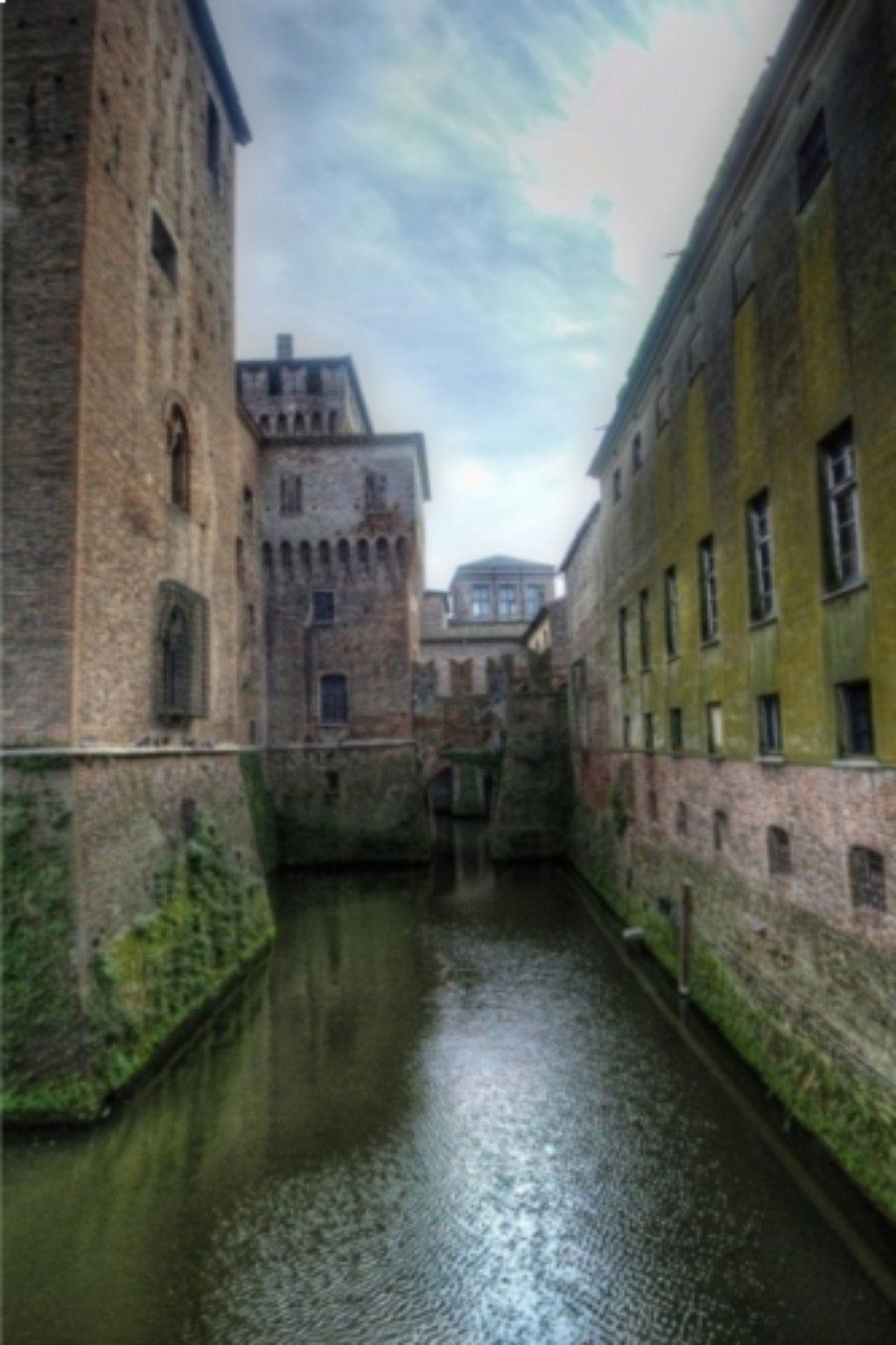 Uno stretto canale tra alti edifici in pietra, con pareti ricoperte di muschio verde e un cielo nuvoloso sopra.