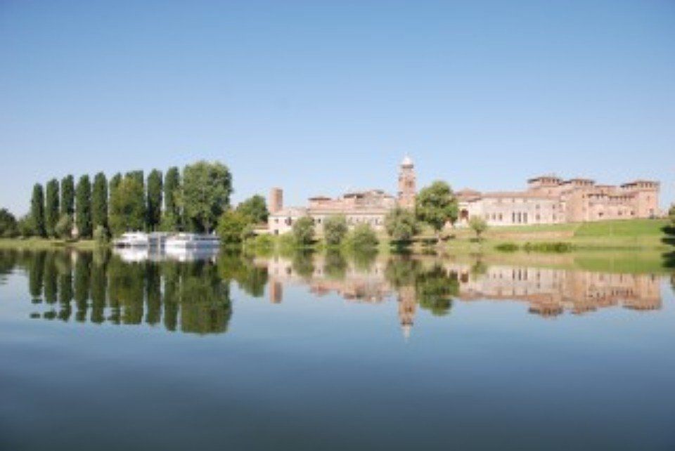 Edificio storico in riva al lago che si specchia nelle acque calme sotto un cielo azzurro e limpido.
