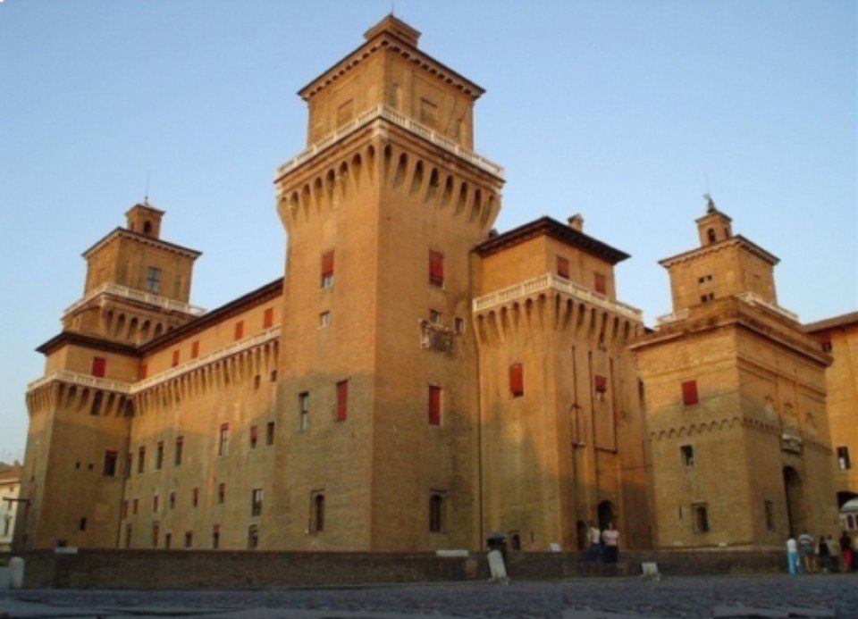 Grande fortezza storica in mattoni di argilla con alte torri quadrate che si stagliano contro un cielo azzurro limpido.