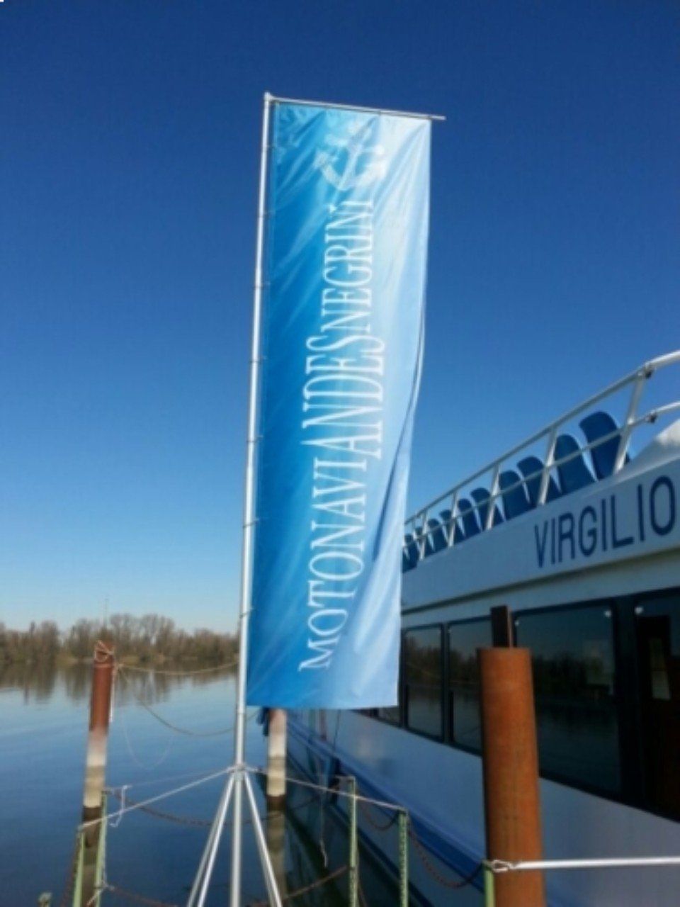 Striscione blu con la scritta “MOTONAVE IDROSCALO” accanto alla barca Viriglio in acque calme sotto un cielo sereno