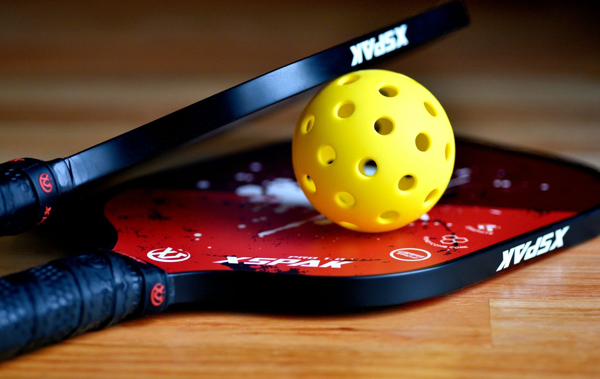 Yellow pickleball and two black paddles on a wooden surface.