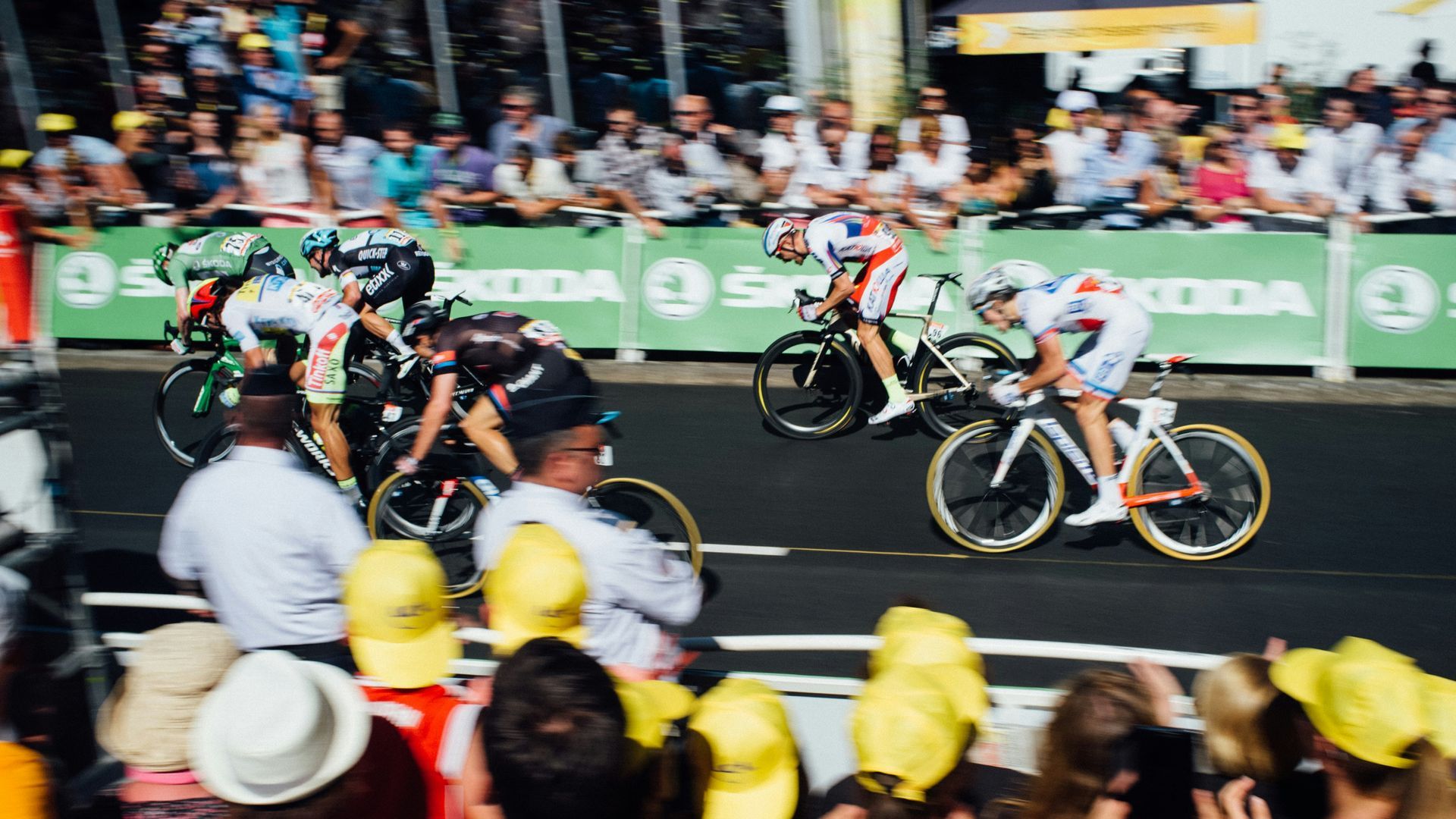 A group of cyclists are riding down a street in front of a crowd.