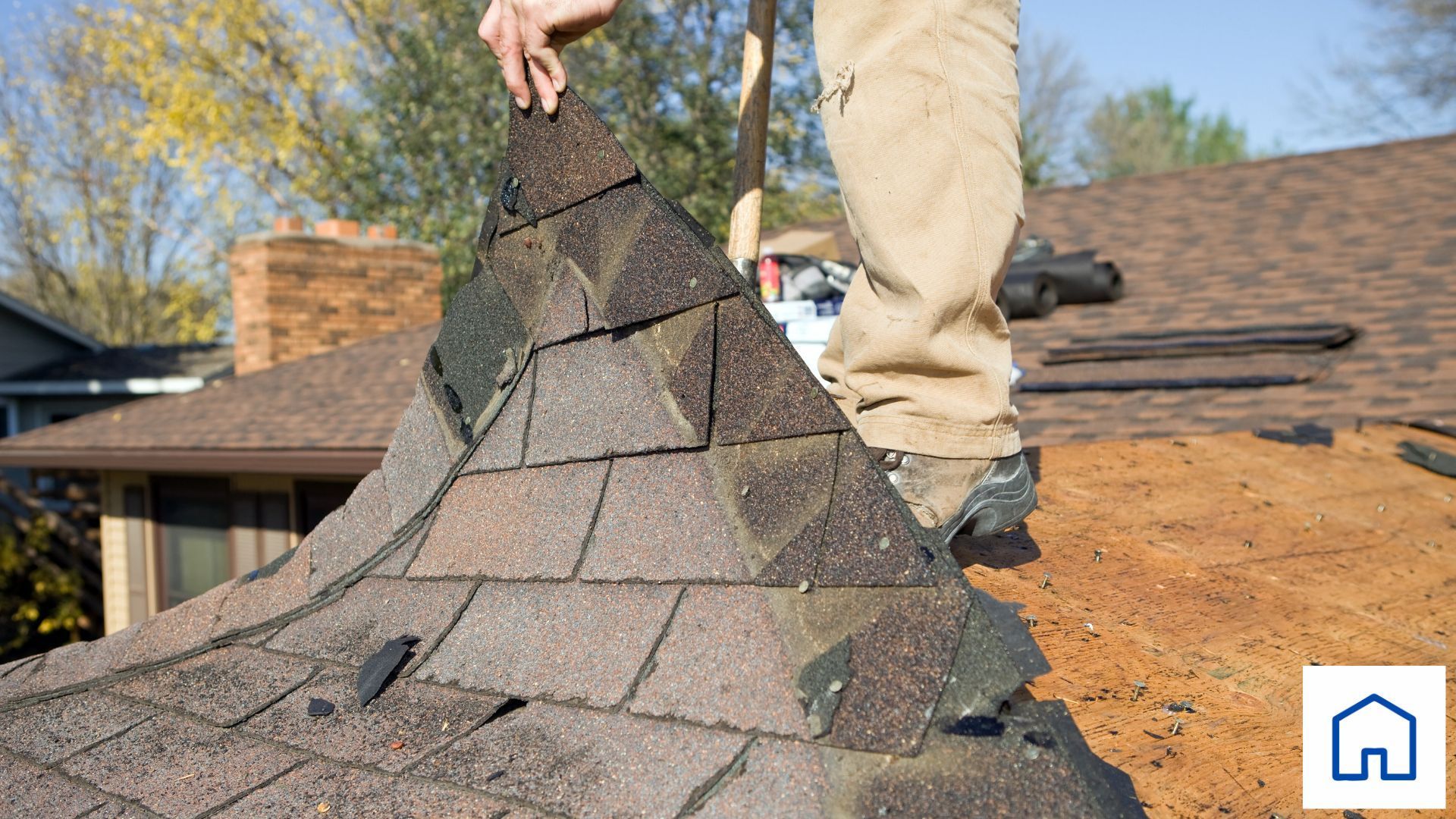 A man is standing on top of a roof holding a piece of shingles.