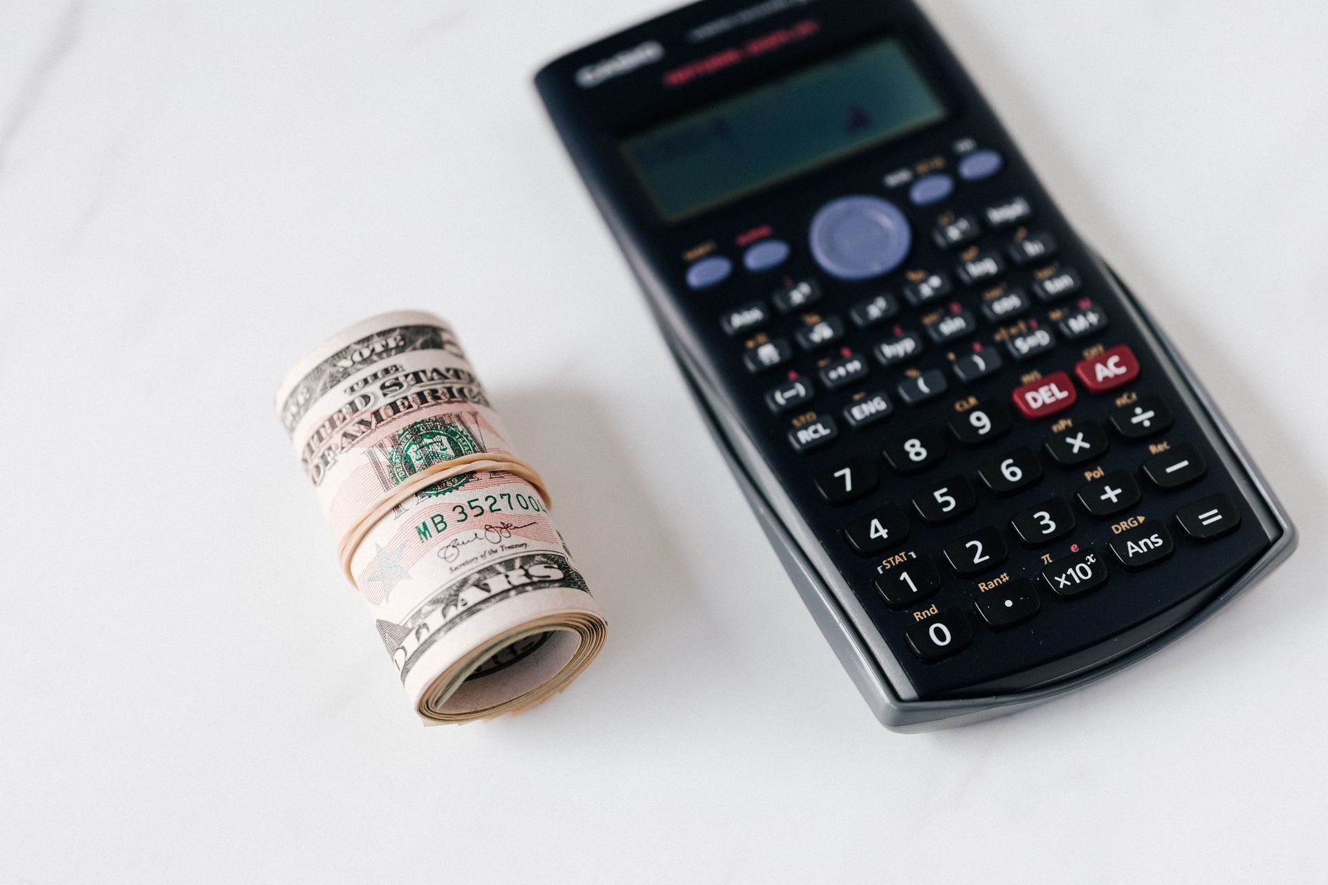 Stack of paper currency beside a calculator on a white surface