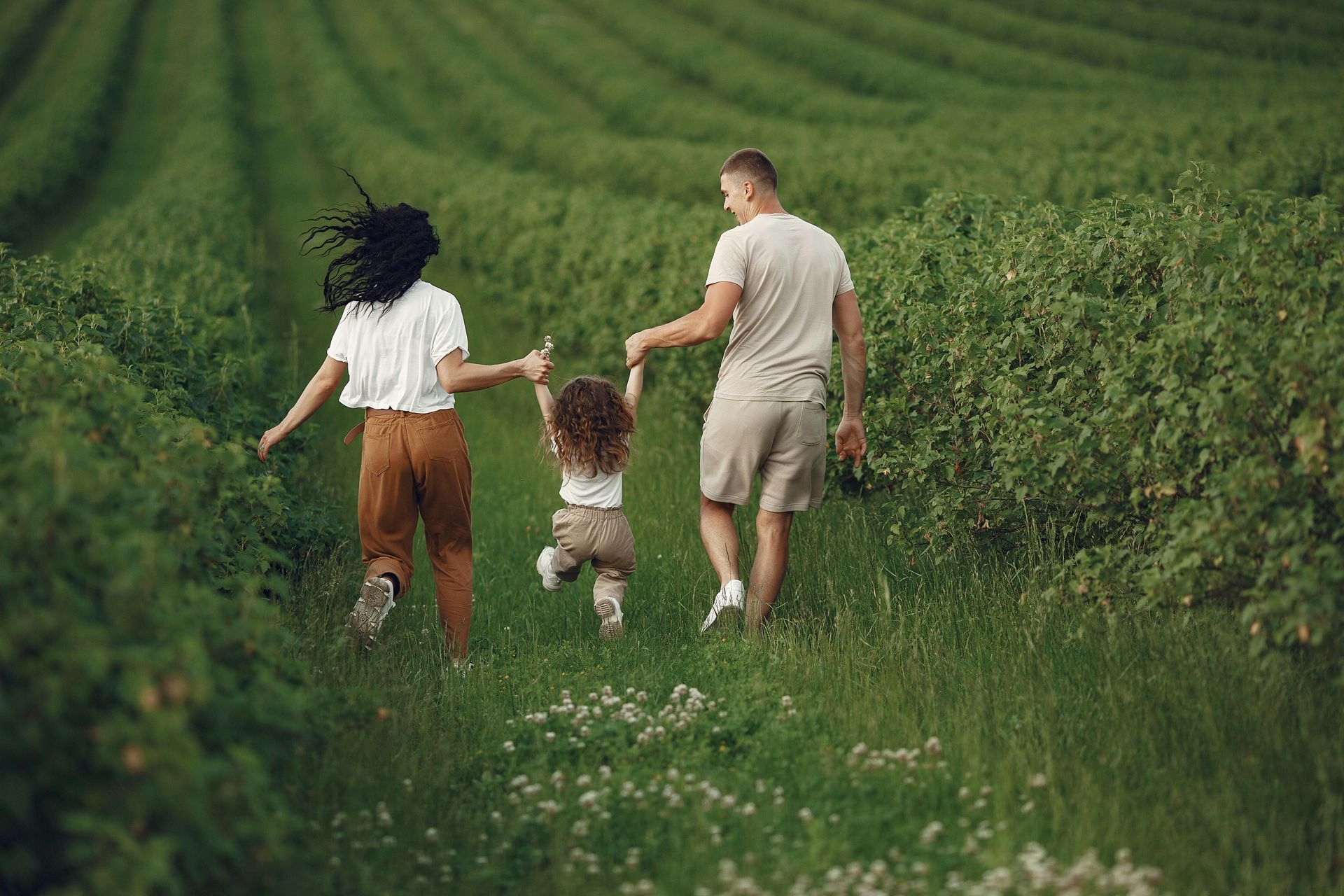 Three people holding hands, walking through a lush green field.