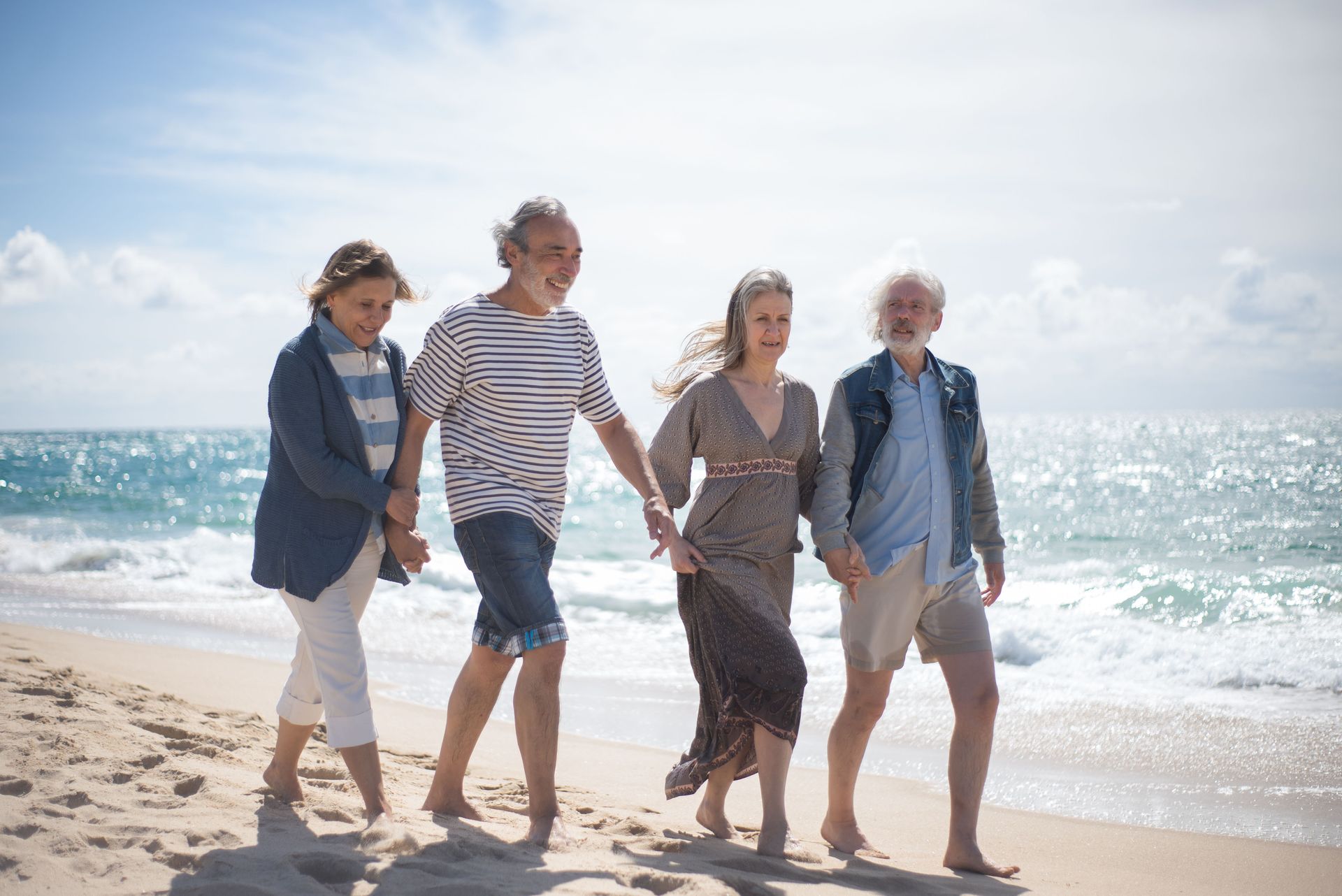 Four people walking barefoot along a sunny beach by the ocean