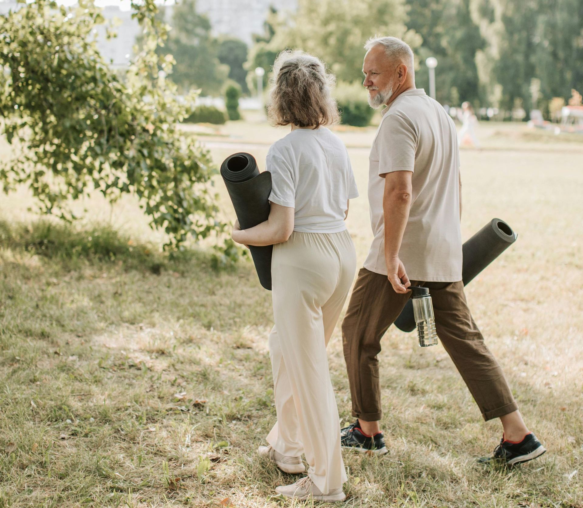 A man and a woman are walking in a park holding yoga mats.