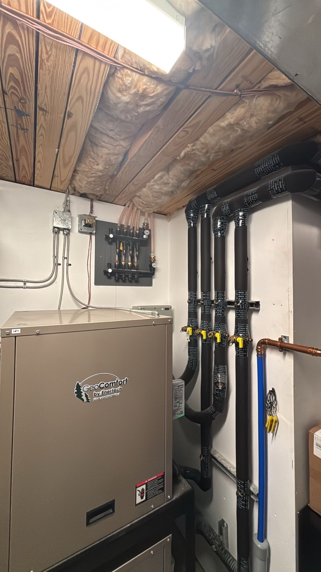 Basement utility room with furnace, pipes, and exposed wood ceiling.