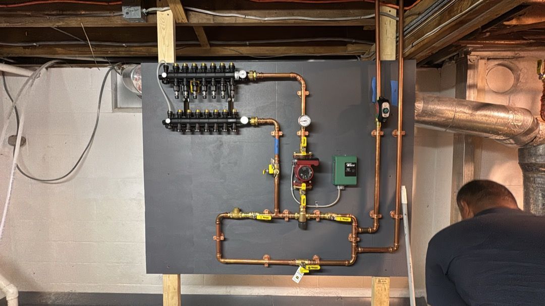 Basement utility wall with copper pipes, valves, and a black manifold; person crouches at right.