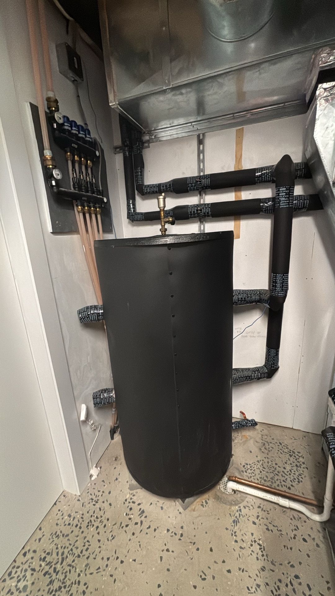Industrial mechanical room with a large black tank and exposed pipes under reflective ductwork