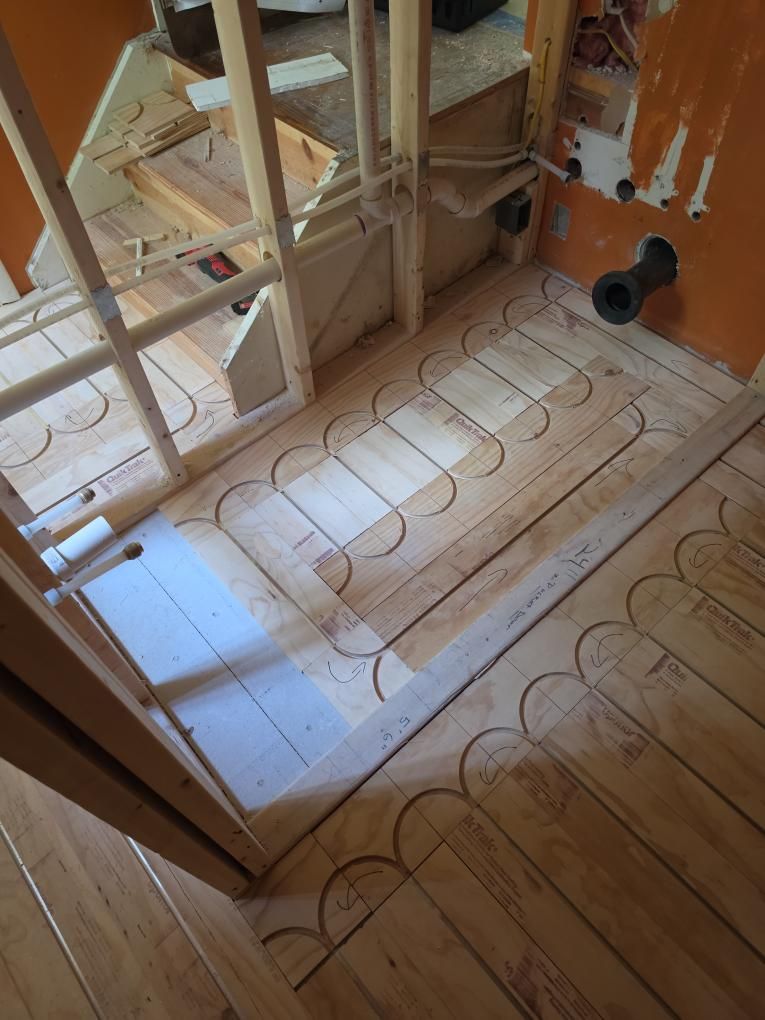 Wood-framed bathroom floor under construction with underfloor heating pipes and plumbing cutouts