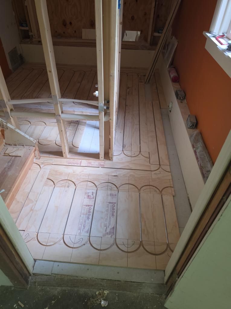 Partially built bathroom floor with radiant heating tubes laid over subflooring and exposed wall studs