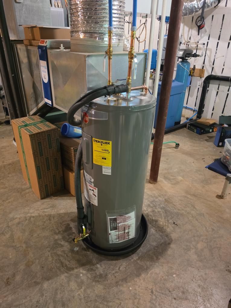 Gray water heater with yellow warning label in a basement utility area, near cardboard boxes and pipes