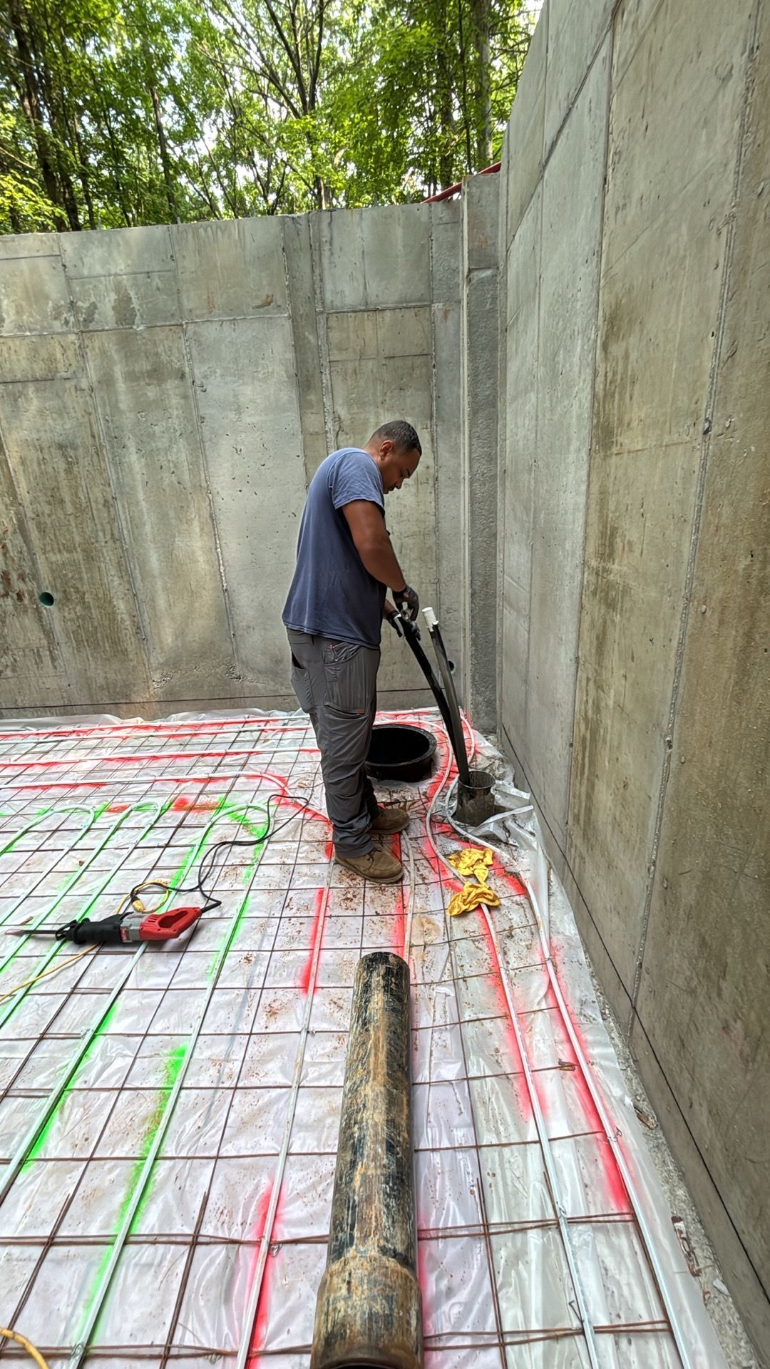 Worker pouring concrete on a rebar grid in a narrow walled trench