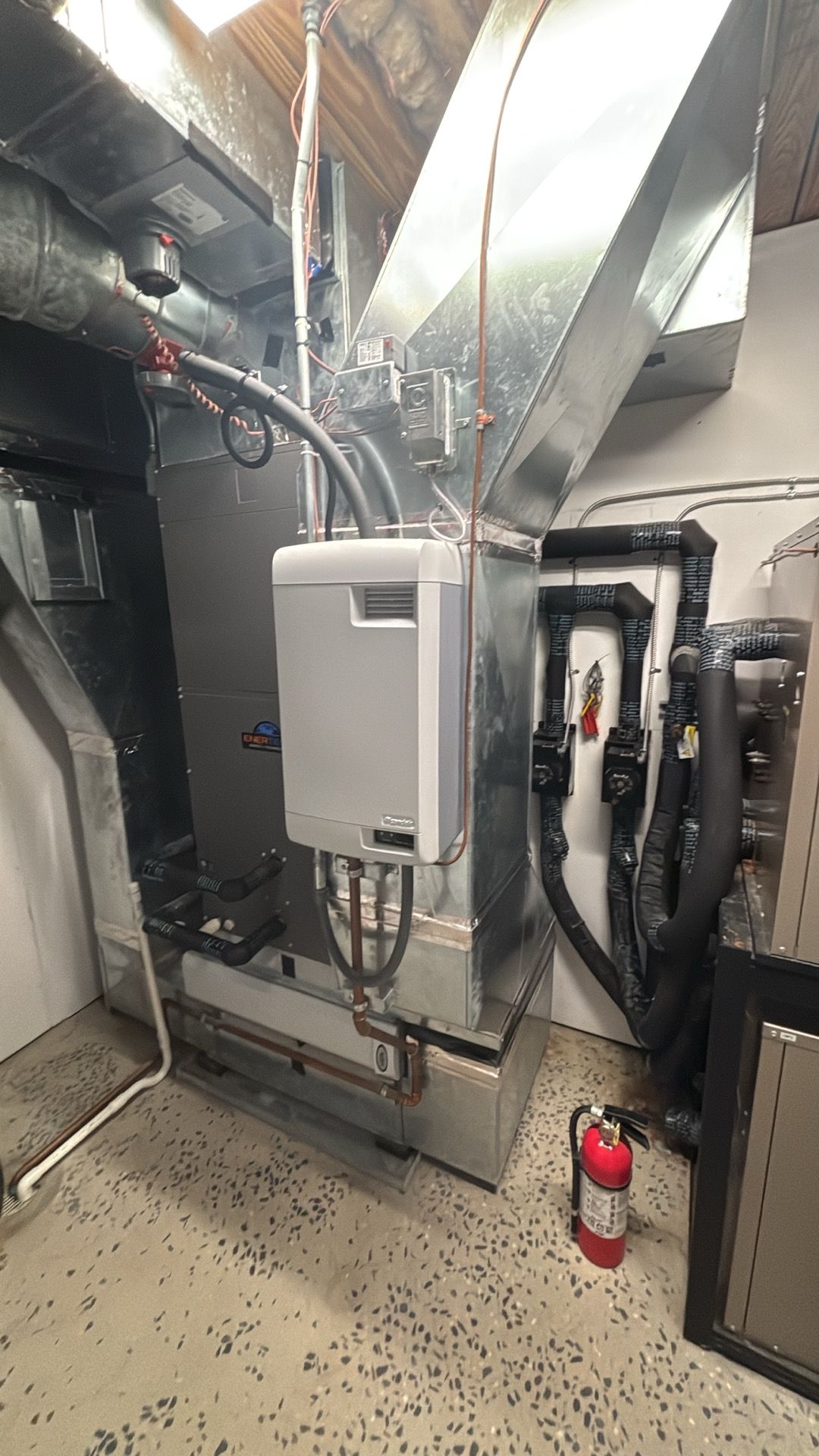 Mechanical room with HVAC equipment, ductwork, and a fire extinguisher on a speckled floor.