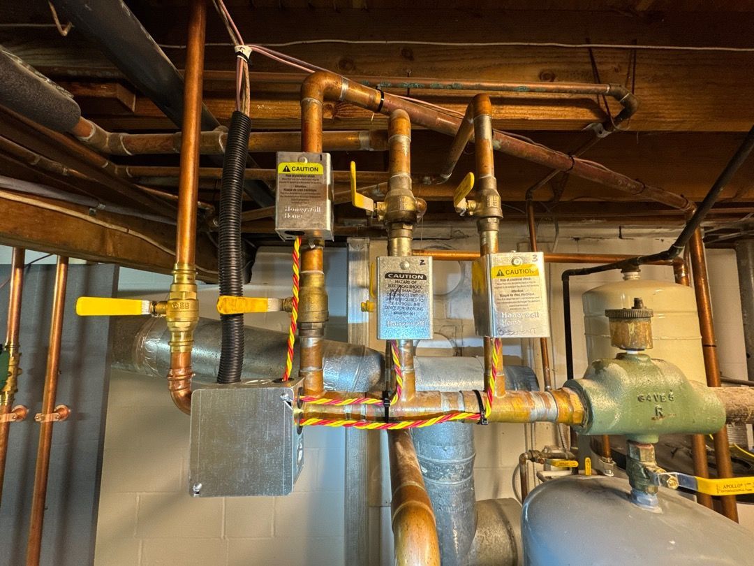 Basement mechanical room with insulated copper pipes, valves, and labeled HVAC equipment overhead