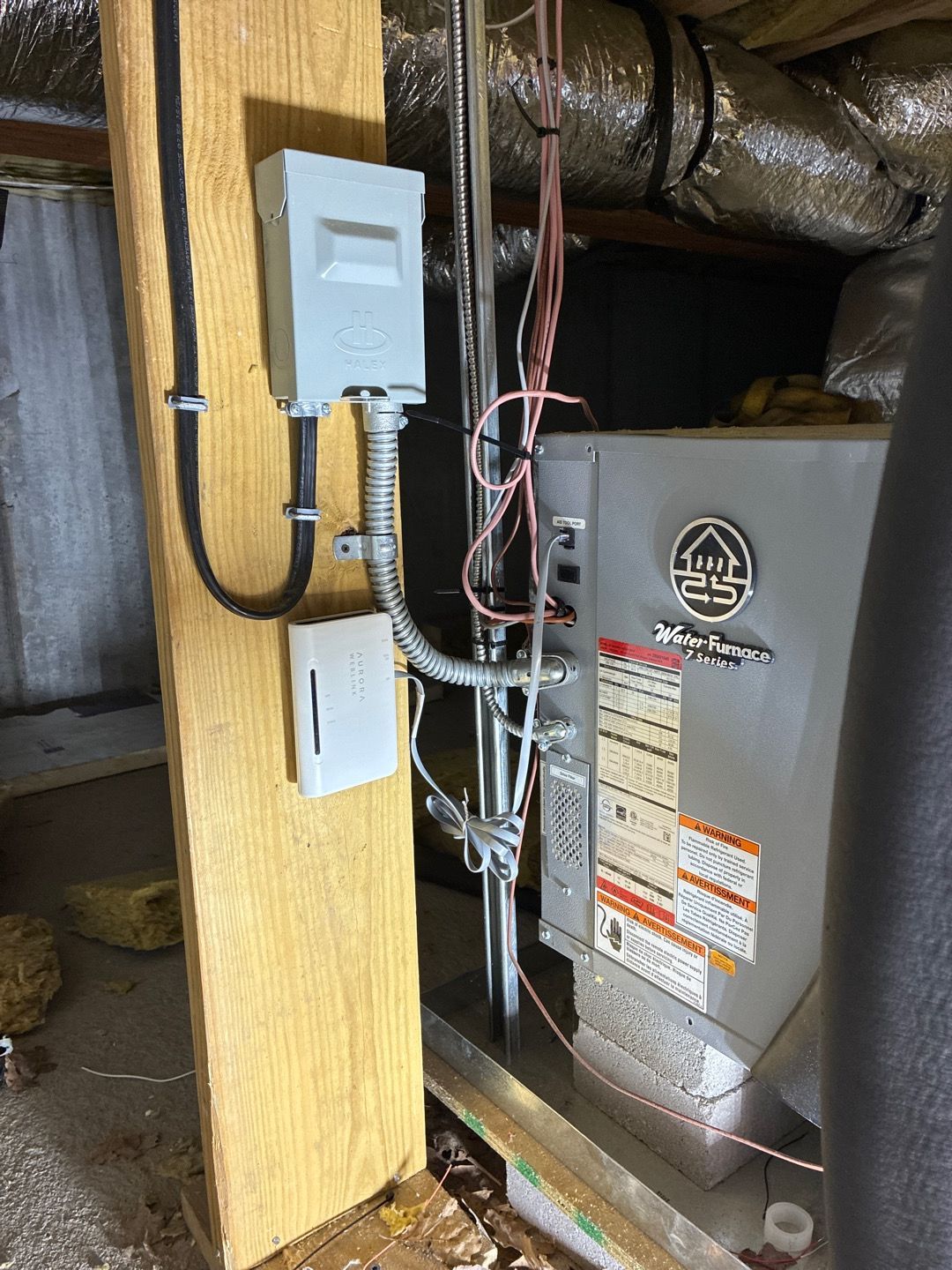 Furnace area in attic with exposed ducts, electrical panels, and wiring beside a wooden support post