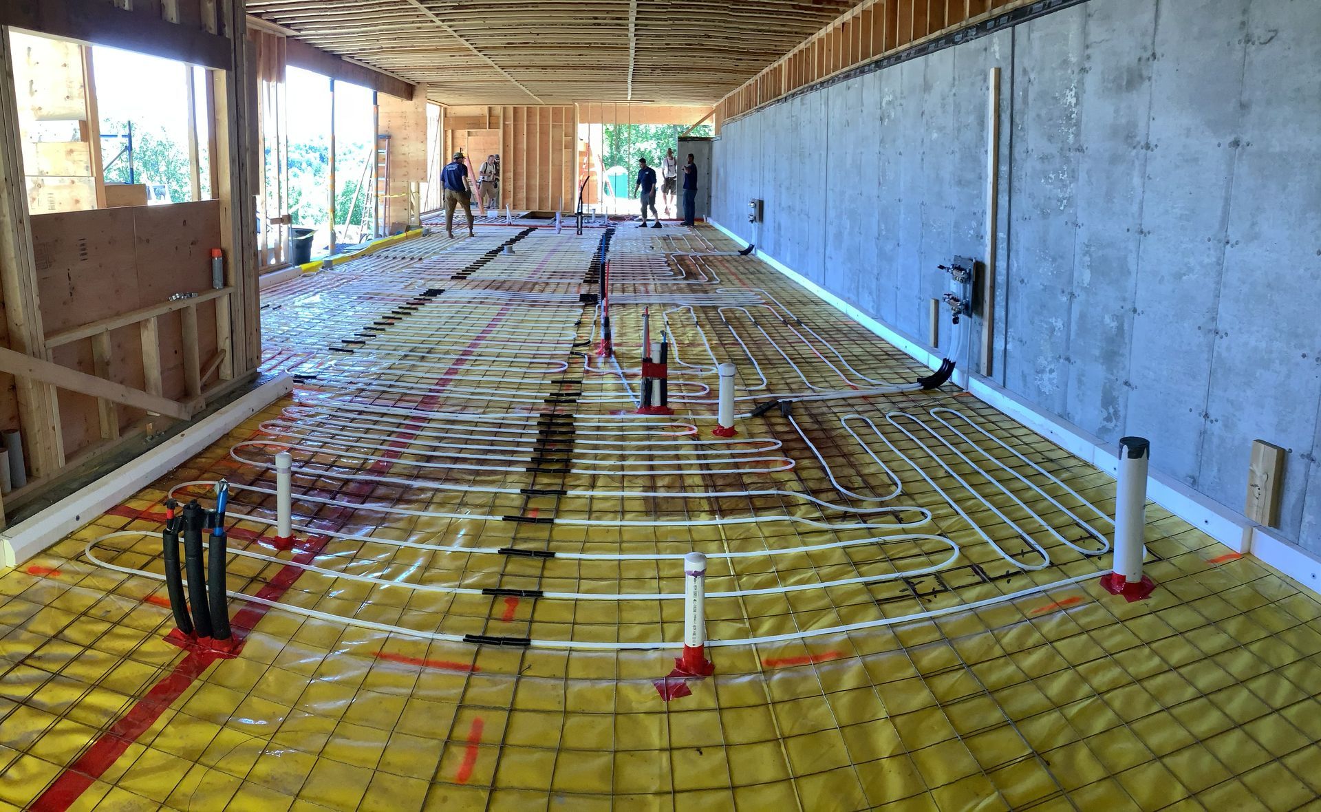 Interior under construction with yellow insulation, exposed framing, and concrete wall along a long corridor