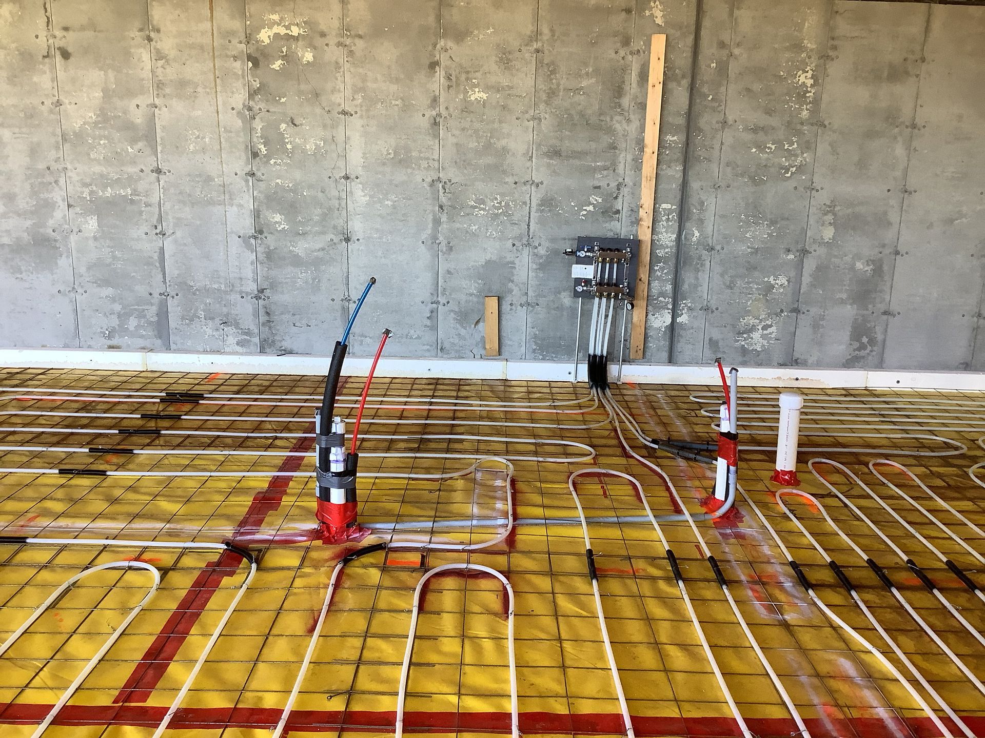 Construction floor with rebar grid, orange safety tubing, and electrical conduits against a concrete wall
