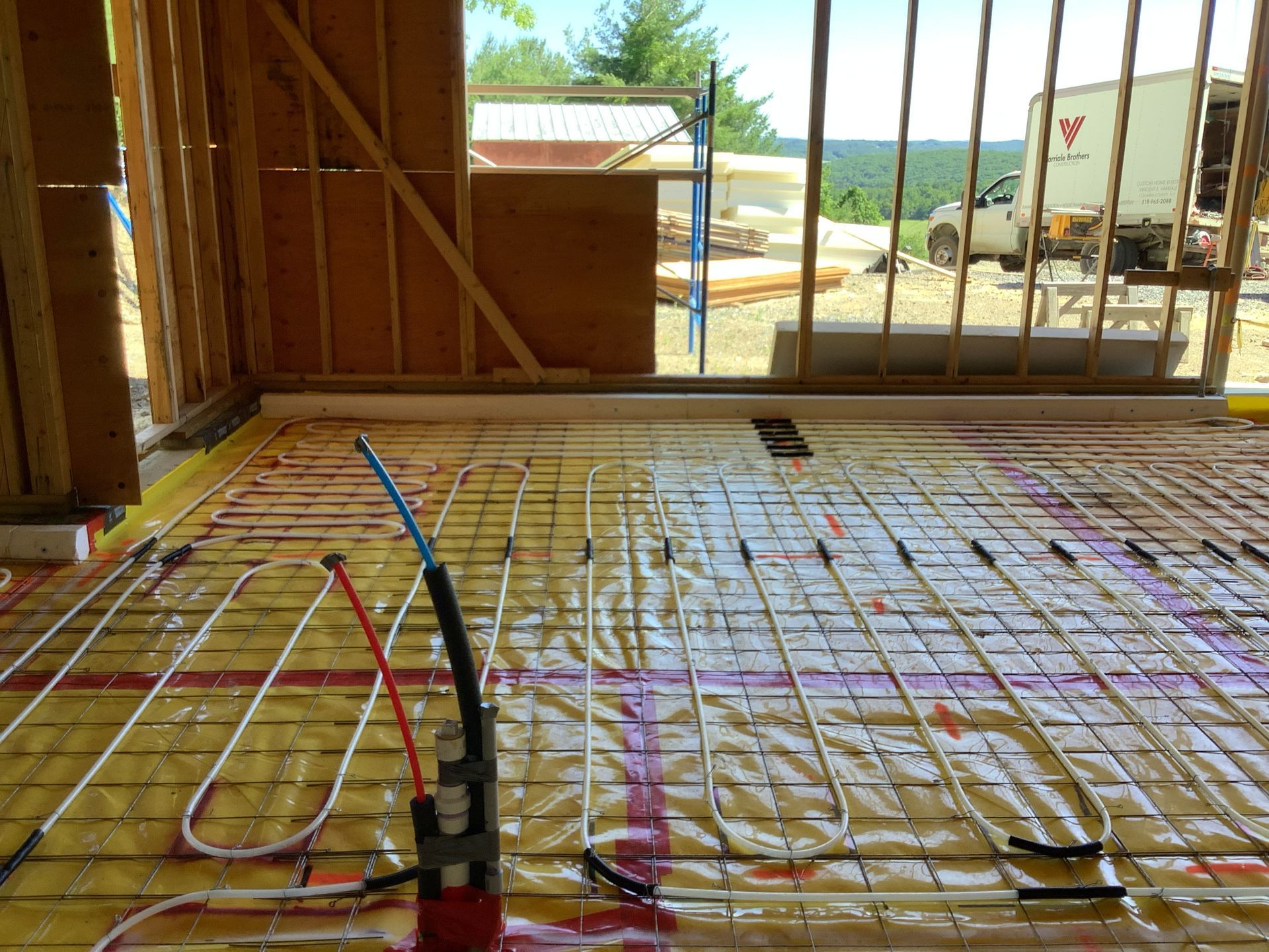 Framed house interior with floor tubing and wiring, looking out to a sunlit waterfront outside.