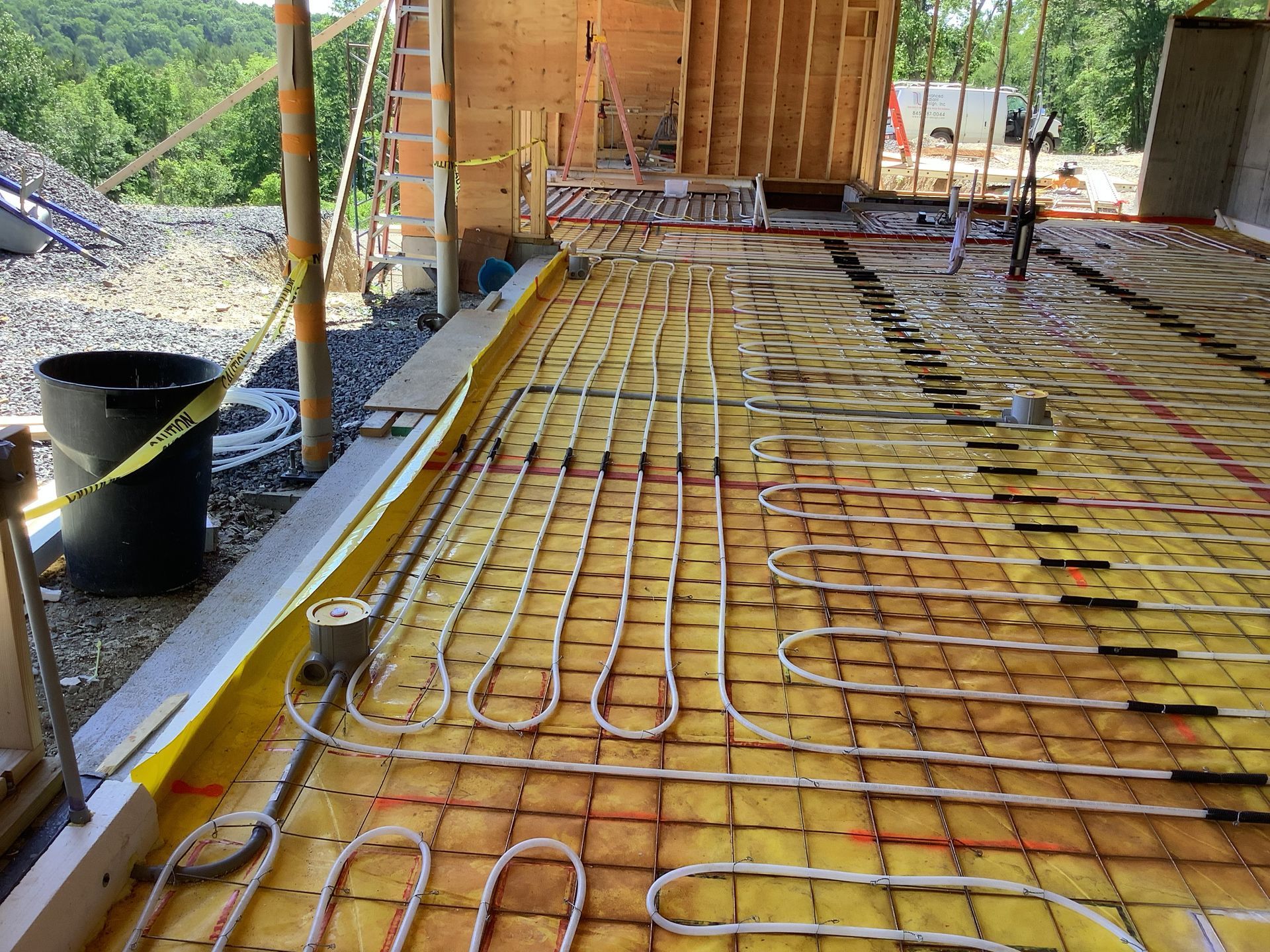 Construction site with floor rebar grid, tubing loops, and wooden framing under a roof.