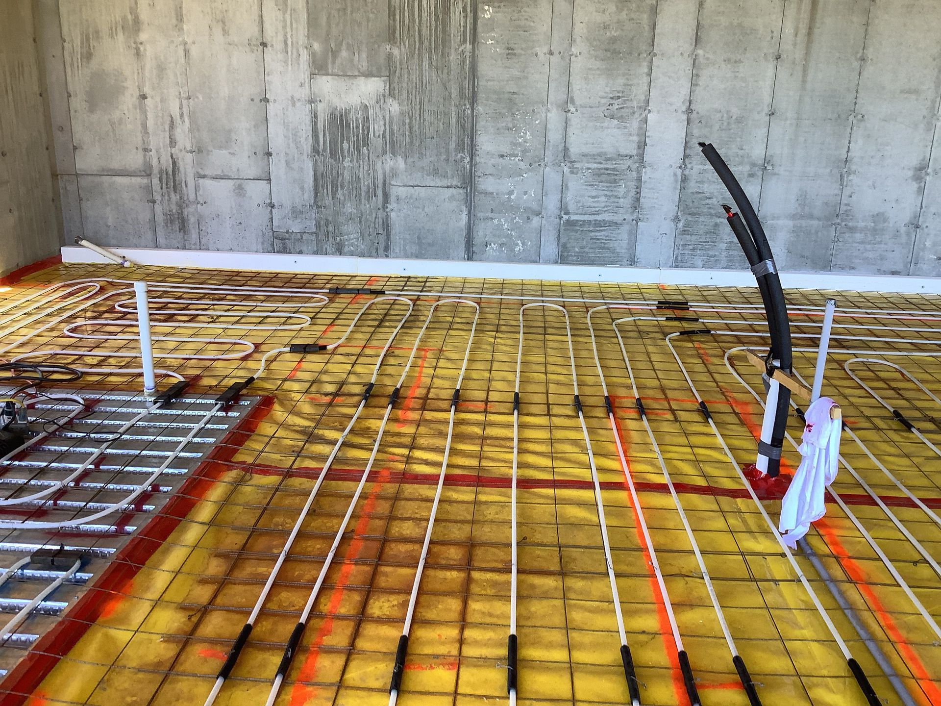 Construction site with rebar grid and bright orange floor slab beside a concrete wall