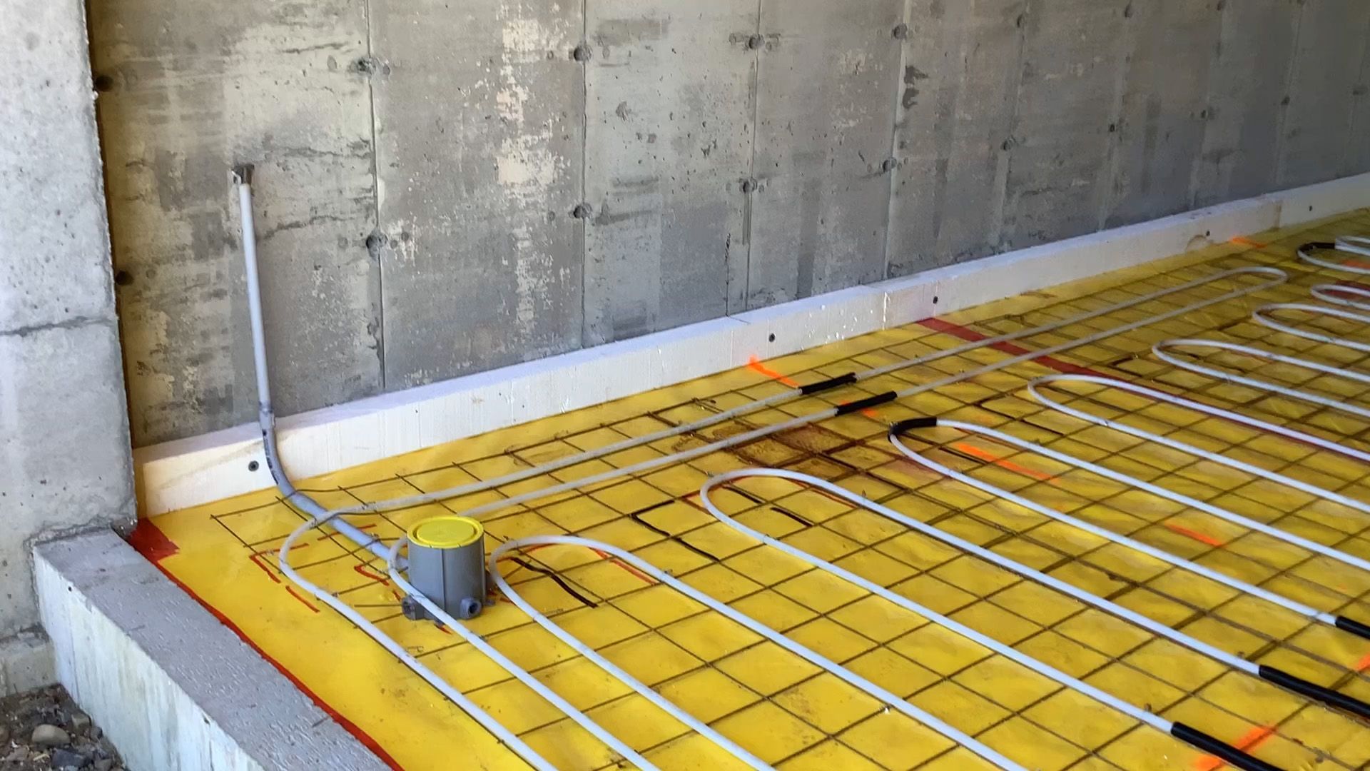 Floor heating pipes laid over yellow insulation in a concrete room under construction